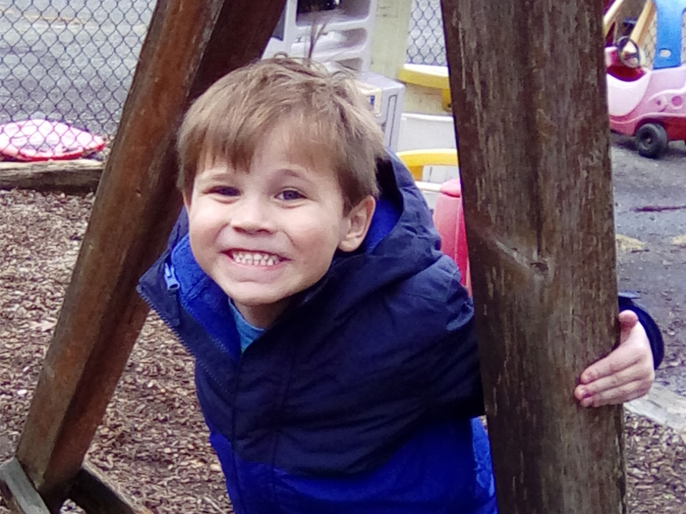 prekindergarten boy smiling big in his blue coat on the playground