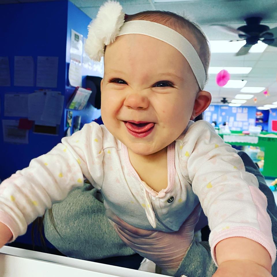 Infant and/or Toddler baby girl smiling through the window with white headband and a pink shirt on.