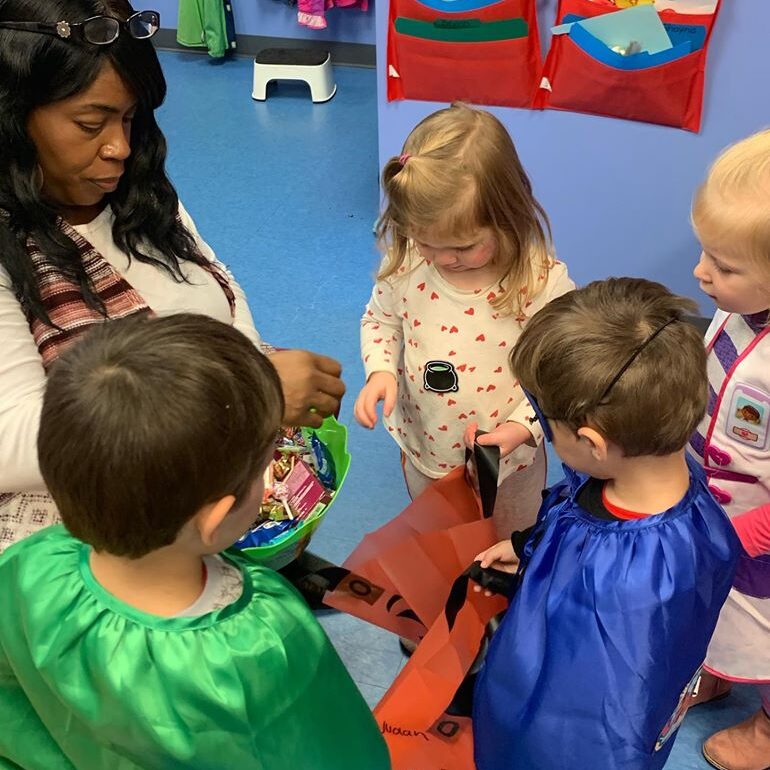 Preschool and toddler students in Halloween Costumes sharing time with Pre-Kindergarten Teacher